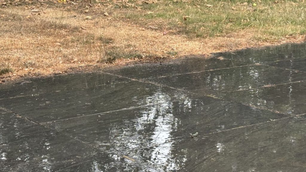 Rain bouncing on dark paving slabs beside the browned edge of the lawn
