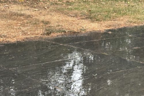 Rain bouncing on dark paving slabs beside the browned edge of the lawn